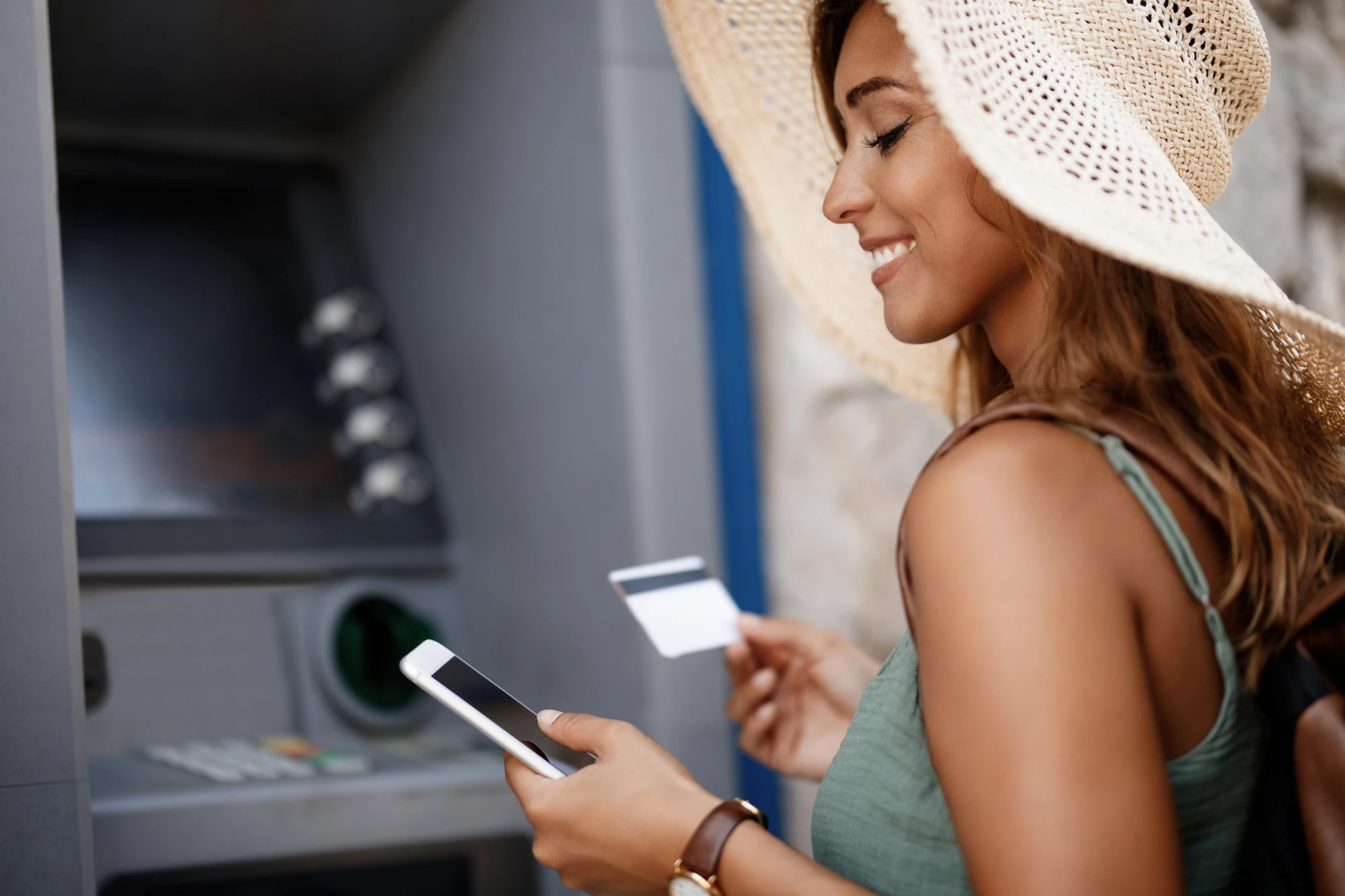 Happy woman using mobile phone while withdrawing cash from an ATM
